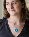 A woman wearing a silver chain necklace with an oval turquoise pendant featuring a black and white graphic design, paired with a black v-neck t-shirt.