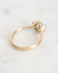 A close-up shot of a gold ring with a unique sculpted setting featuring clear gemstones, resting on a light marble surface.