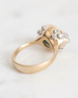 A vintage-style ring with a polished yellow gold band and a cluster of small clear gemstones on a light marble surface.