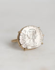 A gold ring featuring an antique silver coin with a profile portrait, set against a plain light gray background.