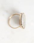 A gold ring with a large, oval, clear stone set in a prong setting, photographed on a light marble surface.