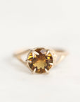 A yellow gold ring featuring a round-cut brown gemstone in a prong setting, photographed against a plain white background.