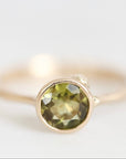 A gold ring with a round faceted olive green gemstone in a prong setting, photographed against a clean white background.