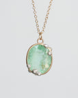 An oval pendant necklace featuring a light green faceted gemstone in a gold-toned setting with textured silver accents, suspended from a delicate gold chain against a light gray background.
