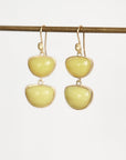 A pair of gold drop earrings with two smooth, pale yellow stone-like oval shapes, hanging from a thin horizontal gold rod against a plain white background.