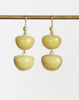 A pair of gold drop earrings with two smooth, rounded pale yellow-green stone segments hanging from gold hooks, displayed against a light gray background.