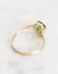 A rose gold ring with a green gemstone, photographed on a light marble surface.