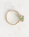 A gold ring with a small green rectangular gemstone, photographed on a light marble-like surface.