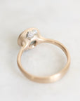A close-up shot of a gold ring with a unique organic-shaped setting featuring small barnacles, resting on a light marble surface.
