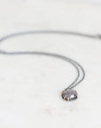 Purple spinel necklace with oxidized chain on marble surface