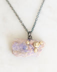 A fossilized opal adorned with gold barnacle details set east west on an oxidized silver chain laid out on a marble background.