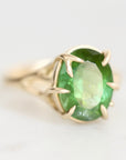 A yellow gold ring featuring an oval-cut green gemstone in a prong setting, photographed on a clean white background.