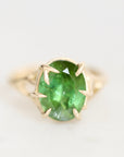 A yellow gold ring featuring an oval-cut green gemstone in a prong setting, shown on a clean white background.