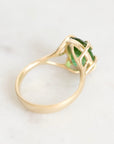 A yellow gold ring with a green gemstone, photographed on a light marble surface.