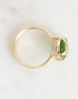 A yellow gold ring with a marquise-cut green gemstone, photographed from a top-down angle on a light, off-white marble surface.
