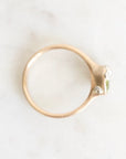 A gold ring with a small green gemstone and clear accent stones, photographed from above on a light marble surface.