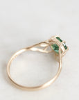 A delicate gold ring featuring a small green rectangular gemstone in a prong setting, resting on a light gray surface.