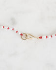 Beaded necklace with red and white beads and a gold clasp on a light gray background