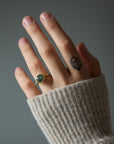 Hand wearing a gold ring with a green Montana sapphire, against a neutral background