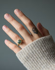 Hand wearing a gold ring with a green Montana Sapphire against a gray background