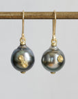 A pair of gold hook earrings with dark gray baroque pearls featuring gold inclusions, hanging from a gold rod against a light gray background.