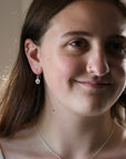 A close-up portrait of a woman wearing a delicate silver hoop earring with a small white bead drop, shown in warm indoor lighting.