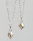 Two silver chain necklaces with oval white pearl pendants, each set with small gold and silver stones, shown against a light gray background.
