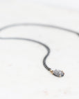 Purple spinel necklace with oxidized chain laying on marble surface