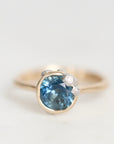 A gold ring featuring a round-cut blue sapphire center stone and small clear accent diamonds, photographed on a clean white background.