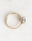 A gold ring with a small cluster of clear gemstones on the side, photographed on a light marble-like surface.