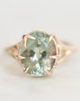 A round-cut light blue-green gemstone ring in a gold prong setting, photographed on a clean white background.