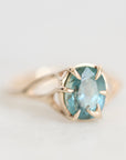 An oval-cut light blue gemstone ring set in a gold prong setting with a gold band, shown on a light gray background.