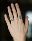A close-up of a person's hand wearing a gold ring with a round turquoise-blue gemstone, set against a dark, blurred background.