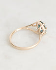 A rose gold ring with a small dark green gemstone, photographed on a light marble surface.