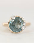 A round-cut light blue gemstone ring in a gold setting with small clear accent stones, photographed on a clean white background.