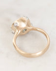 A close-up shot of a gold ring with a unique textured dome setting featuring small clear gemstones, resting on a light marble surface.