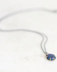 Dark colored opal set in gold prongs with an oxidized silver chain. Laying against a neutral background.