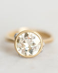 A gold ring with a large round-cut clear gemstone in a bezel setting, photographed on a light neutral background.