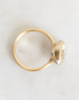 A gold ring with a small cluster of clear gemstones on a light, off-white textured surface.