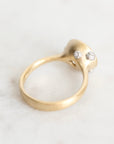 A gold ring with a sculptural, organic-shaped setting featuring two small clear gemstones, resting on a light marble surface.
