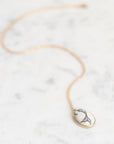 A delicate gold chain necklace with an oval pendant featuring a black and white fish design, displayed on a light gray marble surface.