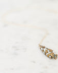 A delicate gold necklace with a teardrop-shaped pendant featuring a white background and a gold floral pattern, resting on a light marble surface.