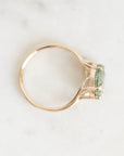 A delicate gold ring with a small green gemstone, photographed from above on a light marble surface.
