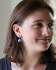 Woman wearing turquoise earring with ship engraving against a blurred indoor background.