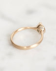 A close-up of a rose gold ring with a small clear gemstone on a light marble surface.