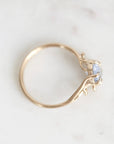 A delicate gold ring with a small light blue gemstone, photographed on a light marble surface.