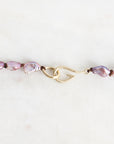 A close-up of a beaded necklace featuring irregular light purple baroque pearls threaded on a gold-toned chain with a decorative twist clasp, set against a plain off-white background.