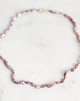 A baroque pearl necklace with irregular, faceted lavender-pink pearls and small gold spacer beads, displayed on a light marble surface.