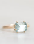 A gold ring featuring a rectangular light blue gemstone in a prong setting, photographed against a clean white background.