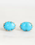 A pair of oval turquoise stud earrings with gold prong settings, displayed on a clean white surface.